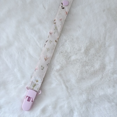 Strap floral rosa e bege com fecho plástico rosa claro sobre superfície branca felpuda