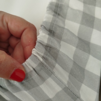 Tecido quadriculado branco e cinzento com elástico na bainha segurado por mão com unha vermelha