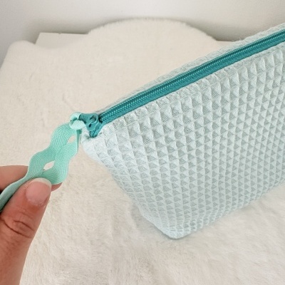 Bolsa azul claro com padrão geométrico e fecho de correr
