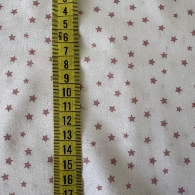 Fita métrica amarela com números pretos sobre tecido branco com estrelas castanhas.