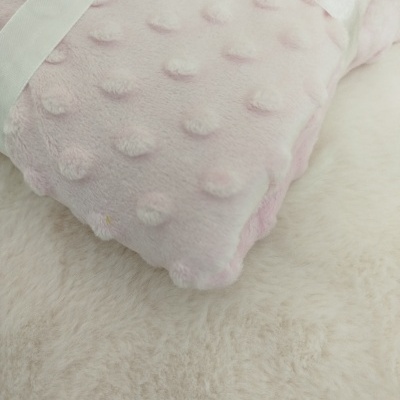 Cobertor rosa claro macio com bolinhas em relevo amarrado com fita branca sobre superfície felpuda bege.