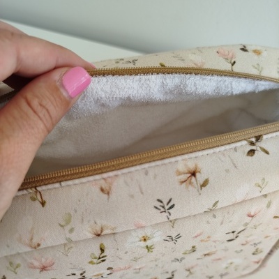 Necessaire bege com padrão floral e fecho de correr a ser aberta