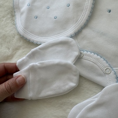 Conjunto de roupa de bebé branca com detalhes azuis e luvas brancas