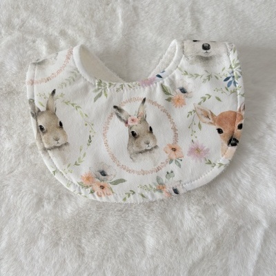 Babador branco com padrão de animais e flores sobre tecido macio branco