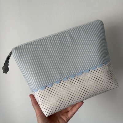 Bolsa de tecido azul com riscas e bolinhas, segurada por uma mão