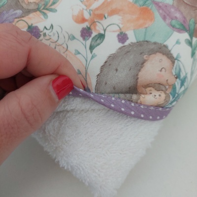 Detalhe de manta ou fralda com padrão de ursos e folhas coloridas e borda roxa com pontos brancos