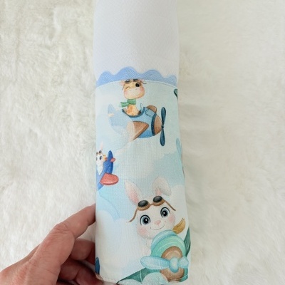 Fralda branca com faixa de tecido colorido e desenhos de girafa e coelho em aviões.