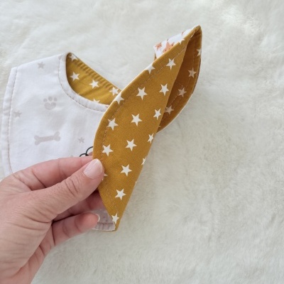 Babete branco com desenhos cinzentos e interior amarelo com estrelas brancas, em superfície branca macia.