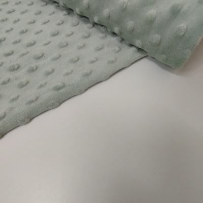 Tecido verde água macio com padrão de bolinhas em relevo sobre superfície branca.
