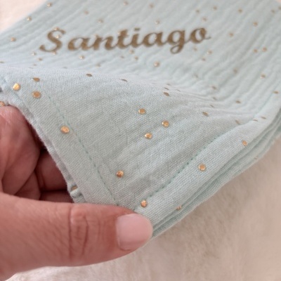 Pano verde-água com pontos dourados e texto Santiago impresso em dourado