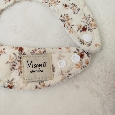 Babete floral com botões de pressão e etiqueta Mamã pintinha sobre fundo branco macio