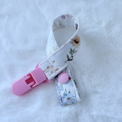 Clipe de chupeta em tecido branco com padrão floral e clip rosa