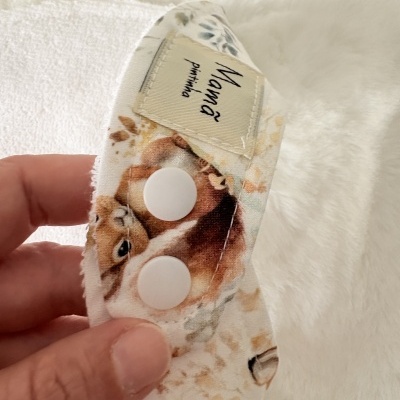 Peça de tecido com padrão de guaxinins, botão branco e etiqueta Mama.
