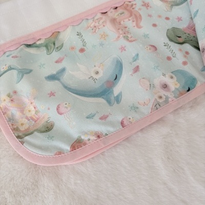 Colchão infantil com padrão de animais marinhos em tons pastel e borda rosa.