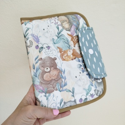 Carteira ou porta documentos tecido com desenhos de animais selvagens em tons pastel e fundo branco.