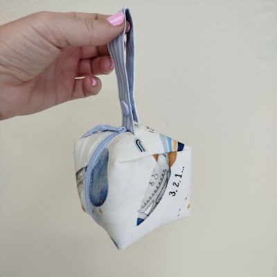 Bolsa pequena de tecido branco com padrão colorido e números segurada por mão feminina