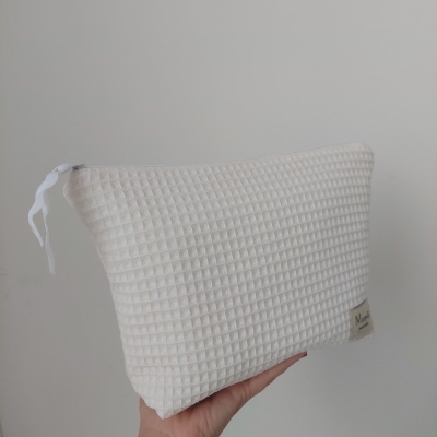 Bolsa branca com padrão quadriculado e fecho de correr, segurada por uma mão