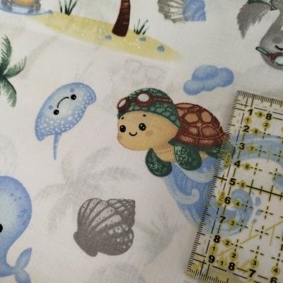 Tecido com estampado infantil de tartaruga e outros elementos marinhos com régua em cm.