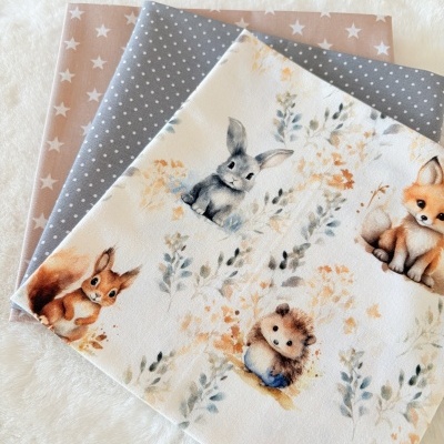 Tecidos dobrados com padrões de estrelas, bolinhas e animais em tons suaves.