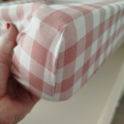 Capa de colchão xadrez rosa e branco com mão segurando canto.
