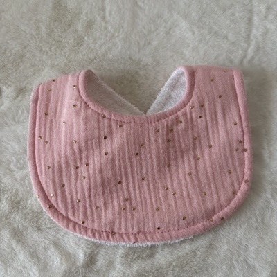 Babete de bebé cor-de-rosa com pontos dourados sobre tecido branco felpudo