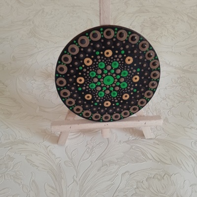 Prato decorativo redondo com padrão de pontos verdes e castanhos num cavalete de madeira