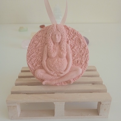 Adorno decorativo cor-de-rosa com mulher grávida em relevo, pendurado em fita e exposto numa mini-palete de madeira clara