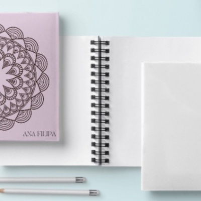 Três cadernos em espiral com capas brancas e lilás, lápis cinza e fundo azul claro.