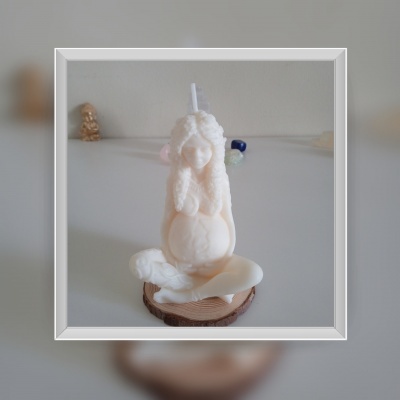 Vela branca com forma de figura humana sentada sobre base de madeira