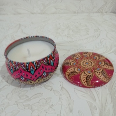 Vela branca em lata metálica decorada com padrões coloridos e tampa removida