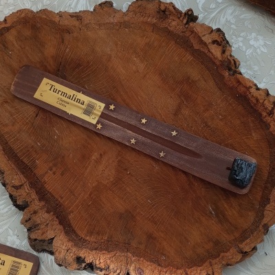 Porta-incenso de madeira castanha com estrelas douradas e etiqueta 'Turmalina' sobre uma placa de madeira