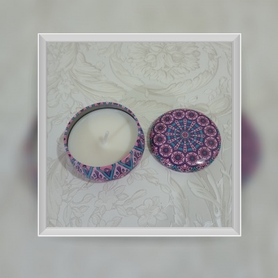 Vela branca em recipiente redondo com tampa estampada e padrão geométrico colorido em fundo claro texturizado