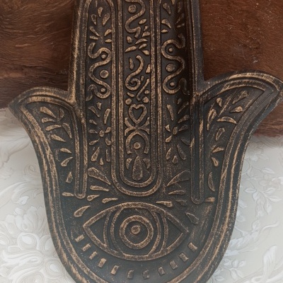 Figura decorativa de mão da Fátima em madeira com gravações e padrão floral de fundo.