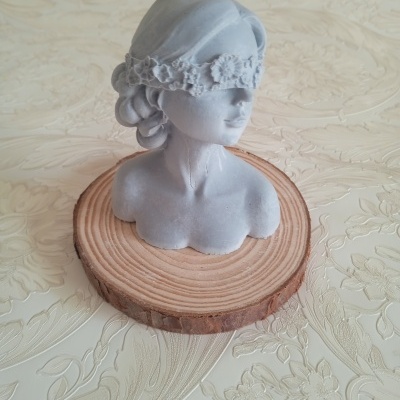 Busto cinza com venda floral sobre base de madeira redonda