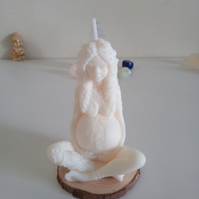 Vela branca em forma de mulher grávida sentada numa base de madeira