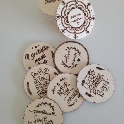 Pequenas placas redondas de madeira com frases e desenhos gravados a laser em português