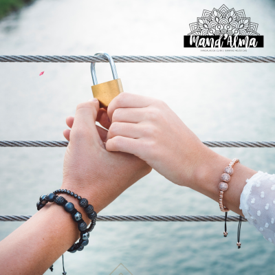 Duas mãos seguram cadeado dourado em cabo de aço com pulseiras visíveis