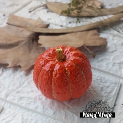 Pequena abóbora laranja artificial com textura sobre superfície branca com folhas secas