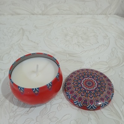 Vela branca em recipiente vermelho com tampa mandala colorida e fundo floral branco