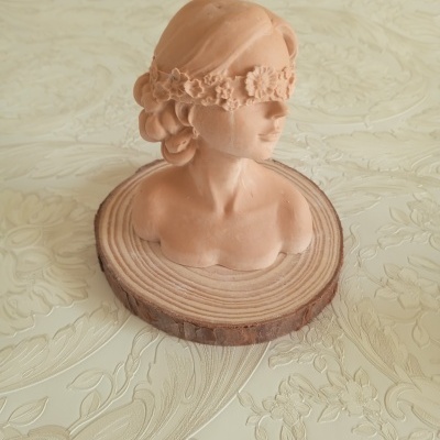 Busto feminino em terracota com faixa floral e base de madeira sobre fundo claro com padrão floral