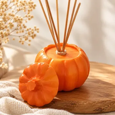 Difusor de essência laranja em formato de abóbora com pauzinhos de madeira sobre tábua de madeira