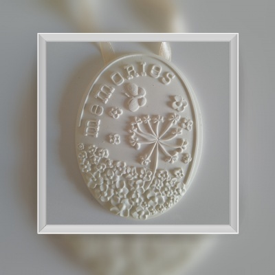 Medalha decorativa branca com relevo de flores e texto 'memórias'