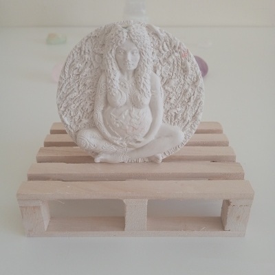 Estatueta branca decorativa de figura feminina grávida em base redonda sobre pallet de madeira.