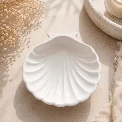Prato branco em forma de concha com flores secas e vela numa tina de pedra ao lado