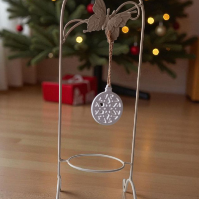 Suporte decorativo branco com borboleta e pendente pendurado, com árvore de Natal iluminada ao fundo