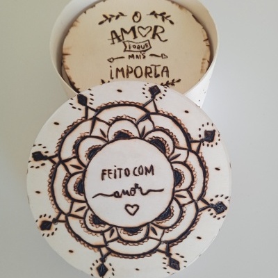 Caixa redonda branca decorada com padrão floral e texto escrito à mão em português.