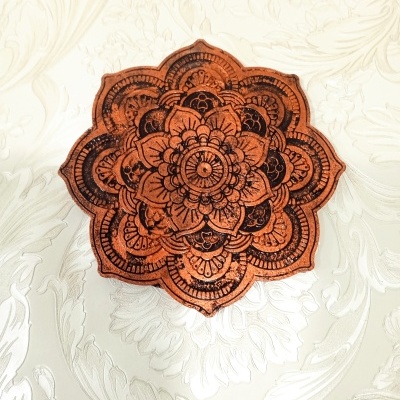 Objeto decorativo mandala em madeira com padrão floral gravado sobre fundo claro com padrão floral