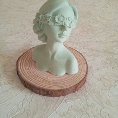 Busto feminino verde claro com faixa floral sobre olhos em base de madeira circular