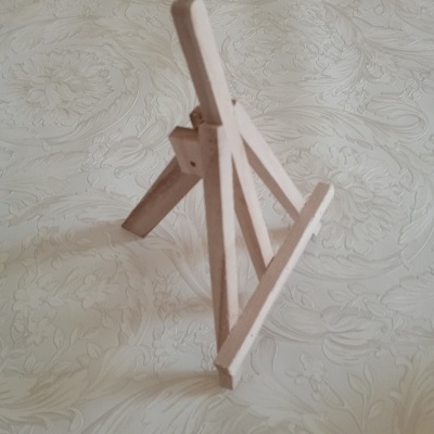 Cavalete de madeira rosa claro com padrão floral em relevo ao fundo.