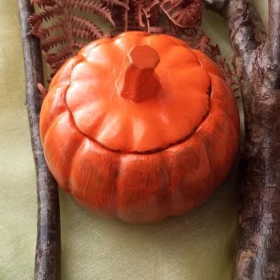 Caixa decorativa laranja em forma de abóbora com galhos secos e folhas ao redor